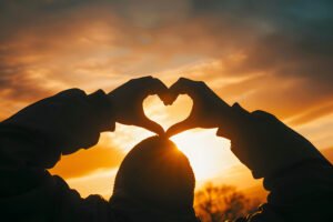 silhouetted hands forming heart shape against glowing sunset creating symbol love hope